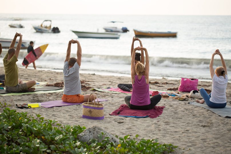 Women doing yoga exercises or supported pigeon pose on an empty beach