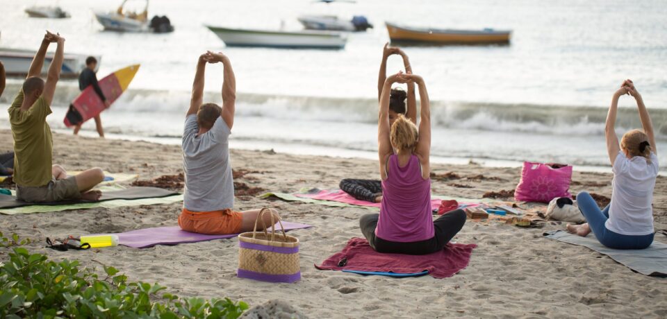 Women doing yoga exercises or supported pigeon pose on an empty beach